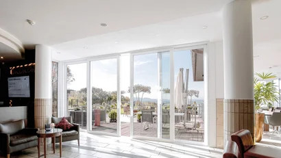 Lichtdurchfluteter Innenraum mit Glas-Schiebetüren zu einer Terrasse mit Stühlen und Pflanzen