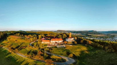 Luftbild eines Schlosses auf einem bewaldeten Hügel mit einer Stadt im Hintergrund