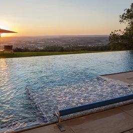 Infinity-Pool bei Sonnenuntergang mit Liegestühlen und Regenschirm