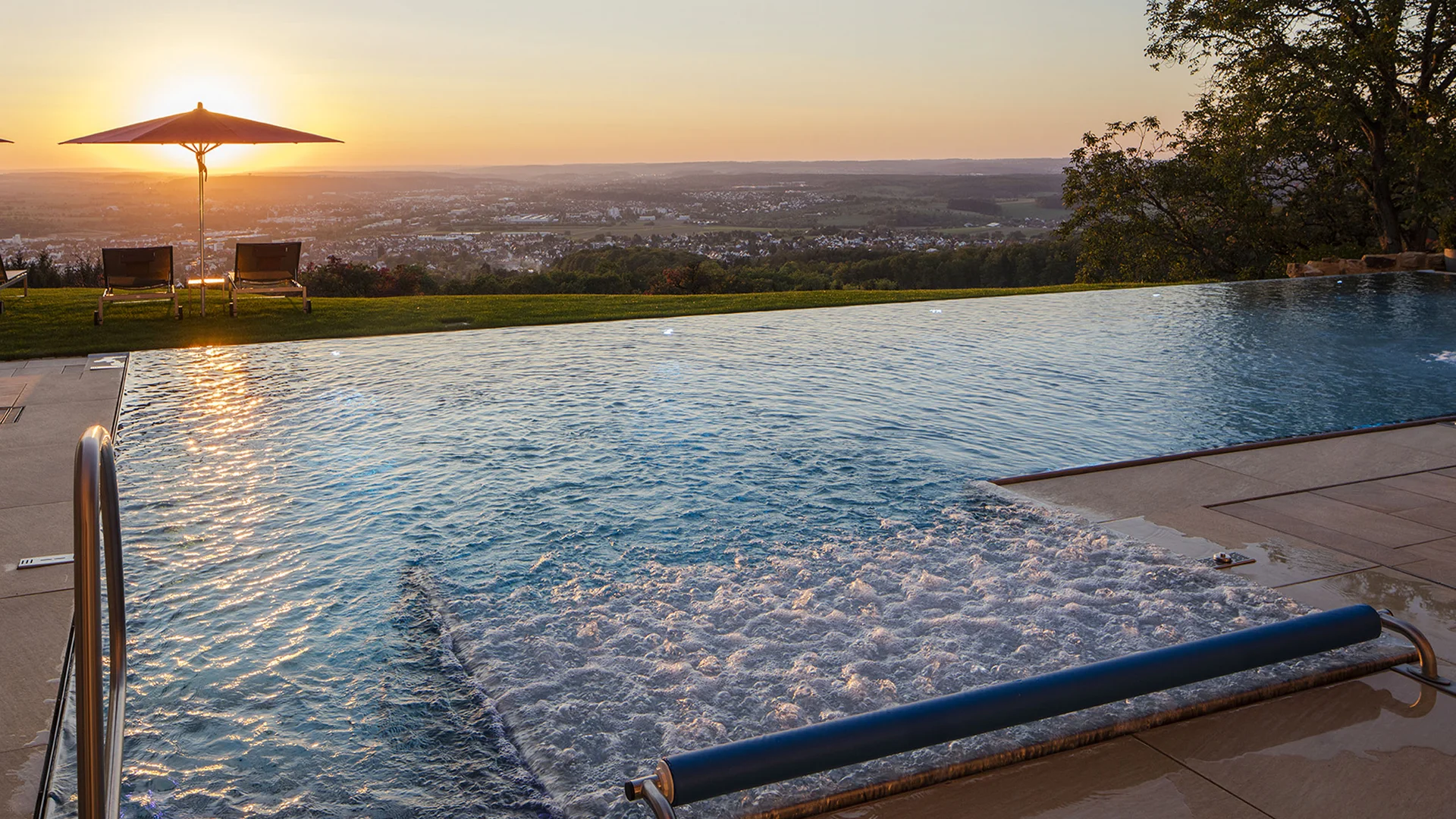 Infinity-Pool bei Sonnenuntergang mit Liegestühlen und Regenschirm