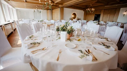 Fein gedeckter Hochzeitstisch mit weißen Stühlen und Blumen in einem festlichen Saal