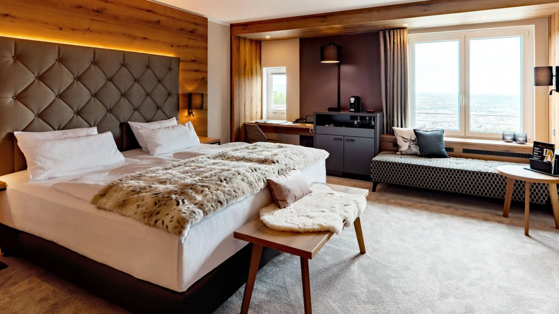 Modernes Hotelzimmer mit Doppelbett, großem Fenster und gemütlicher Sitzbank