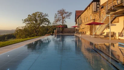 Infinity-Pool neben einem Steinbau mit Sonnenschirmen und Blick auf Landschaft