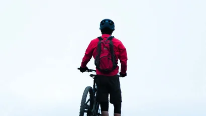 Mountainbiker in roter Jacke steht auf einem Hügel mit seinem Fahrrad