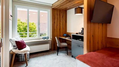 Kleines Hotelzimmer mit Fenster, Schreibtisch, Stuhl, Fernseher und Bett