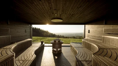 Sauna mit Holzsitzen und Aussicht auf eine grüne Landschaft bei Sonnenuntergang