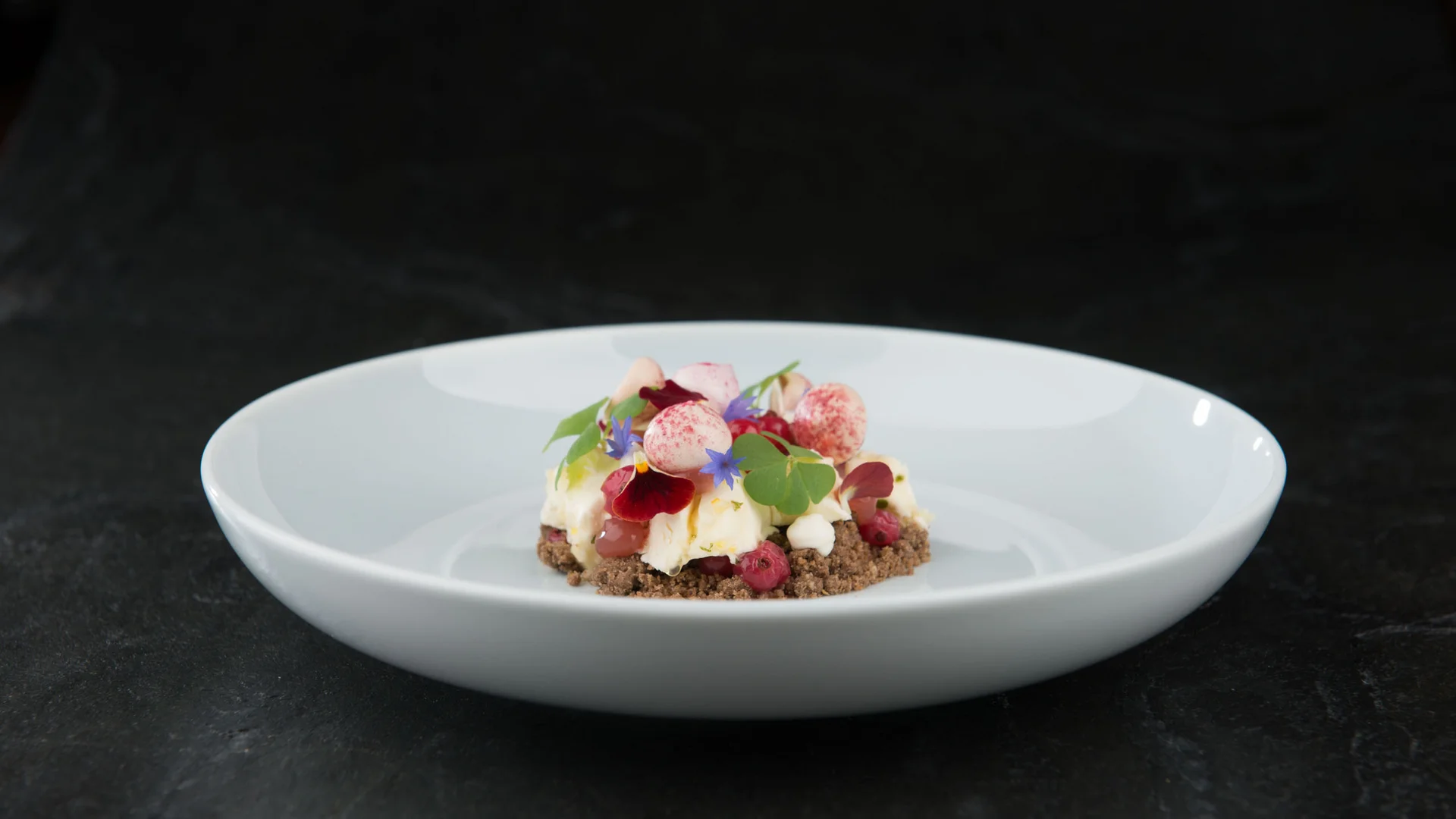 Kreatives Dessert mit essbaren Blüten und roten Beeren auf weißem Teller