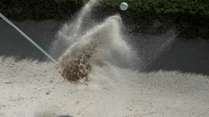 Golfball fliegt aus Sandbunker mit aufwirbelndem Sand